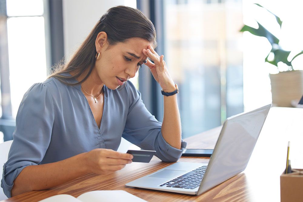 frustrated woman in front of computer looking at credit card in her hand