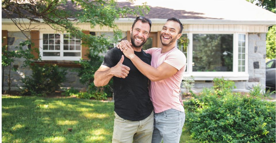 same sex couple standing in front of their home smiling